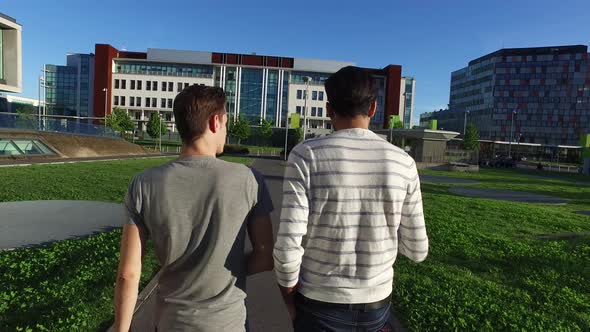 4k back view two young multi ethnic men outdoor walking using smart phone having conversation