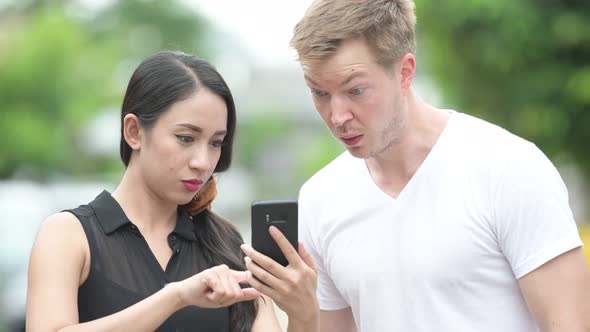 Young Multi-ethnic Couple Using Phone Together in the Streets Outdoors