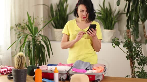 Travel woman packing suitcase, check things on the smartphone