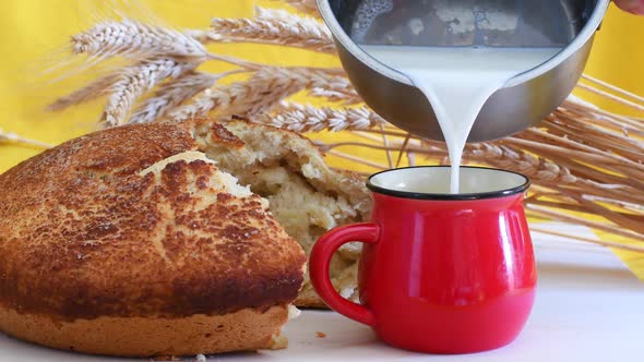 Fresh baked homemade hot bread and pouring milk in a red mug.