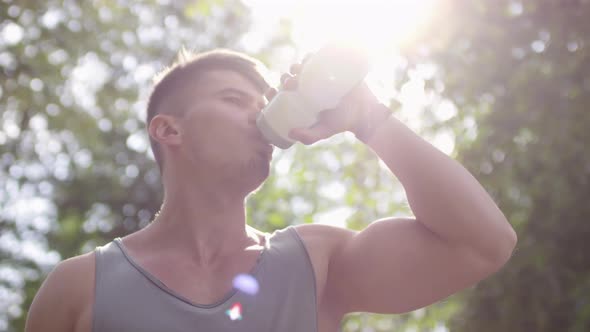 Muscular Man Drinking Water after Exercising in Park