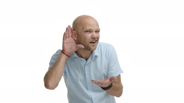 Adult Bald Bearded Guy with Blue Shirt Looking Confused with Hand Near Ear Cant Hear you Asking to