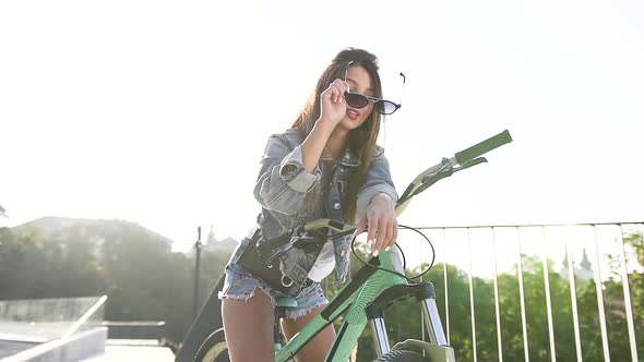 Young Girl in Fashion Jeans Clothes Wears Stylish Glasses Sitting on the Bicycle