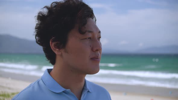 Portrait of a Middleaged Asian Man in a Blue Shirt Standing on the Beach By the Sea Against the