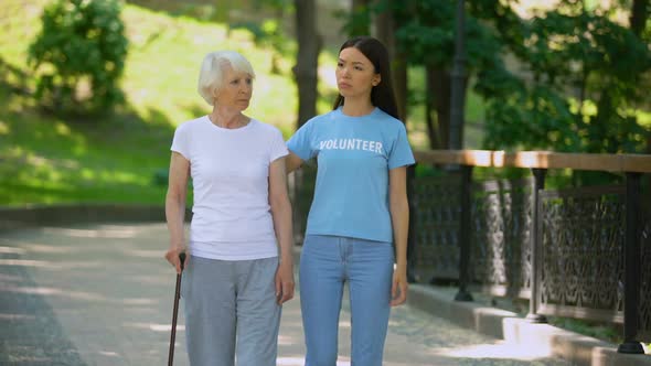 Depressed Mature Woman With Walking Stick and Female Volunteer in Garden, Rehab