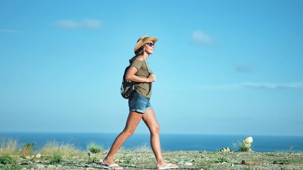 Backpacker Hiker Woman in Sunglasses and Hat Walking on Edge of Mountain Over Sea Side View