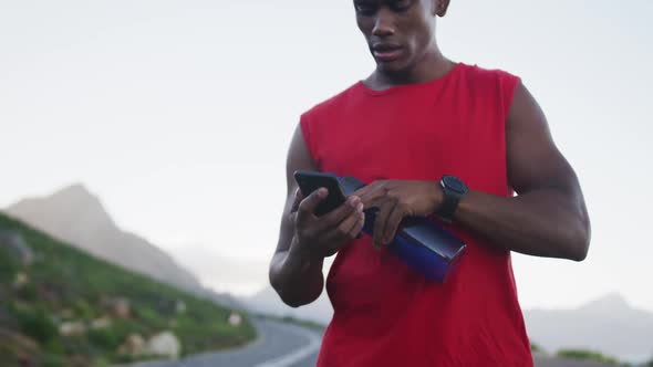 African american man holding water bottle using smartphone on the road