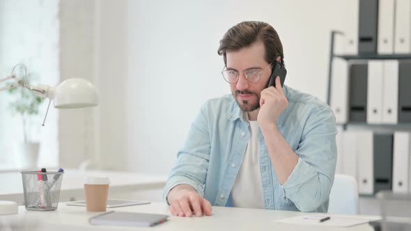 Angry Young Man Talking on Smartphone at Work