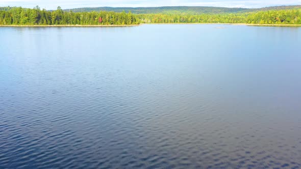 Early fall aerial footage of remote lake in northern Maine flying low over the water towards shore