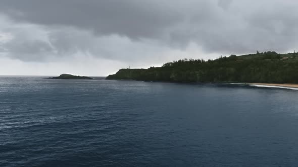 Aerial shot over the ocean near a tropical island in the rain in Kauai, Hawaii, USA