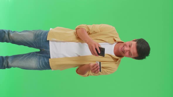 Happy Asian Man Using Mobile Phone With Credit Card For Shopping Online In The Green Screen Studio