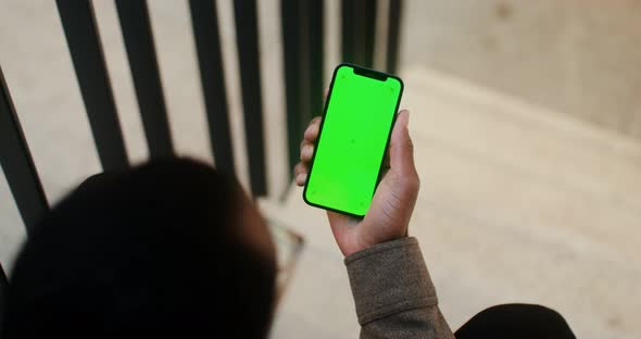 An African American Man Holds a Mobile Phone with a Green Screen in His Hand
