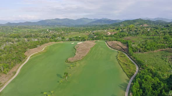 Aerial backwards shot of large Golf CLub with grass fields surrounded by mountains on Dominican Repu