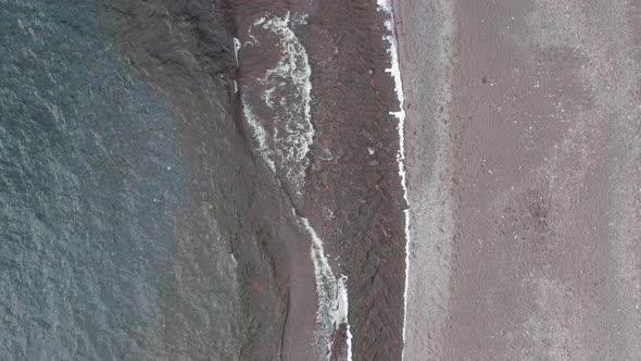 aerial drone view looking down on grey beach with waves of lake superior lapping on shoreline gettin