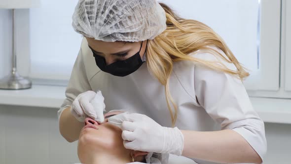 Doctor Beautician in a Black Mask Makes Cleaning the Face of a Young Woman