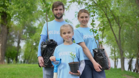 Parents and Child in Volunteer T-Shirts Holding Potted Trees Nature Conservation