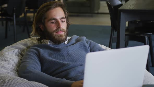 Caucasian businessman sitting on pouf using a laptop in modern office