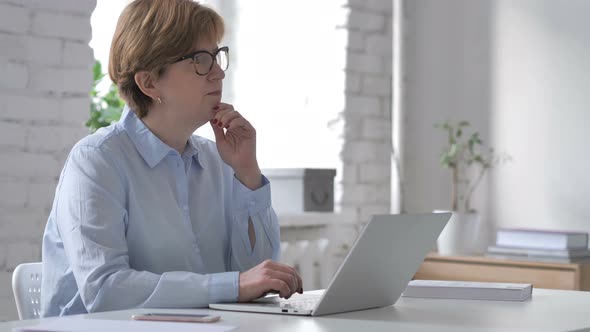 Pensive Old Woman Thinking and Working on Laptop