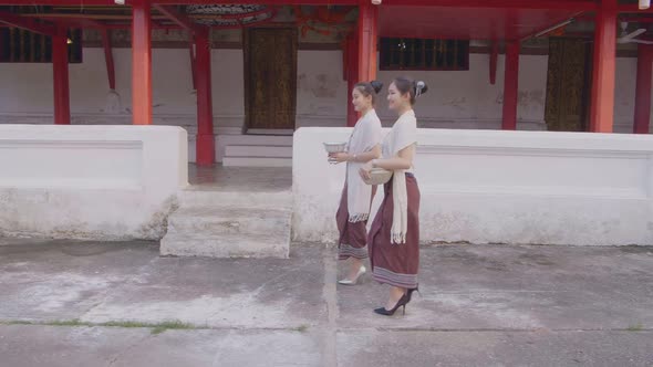 Girls In Thai Traditional Dress Walking Near Temple With The Water Bowl