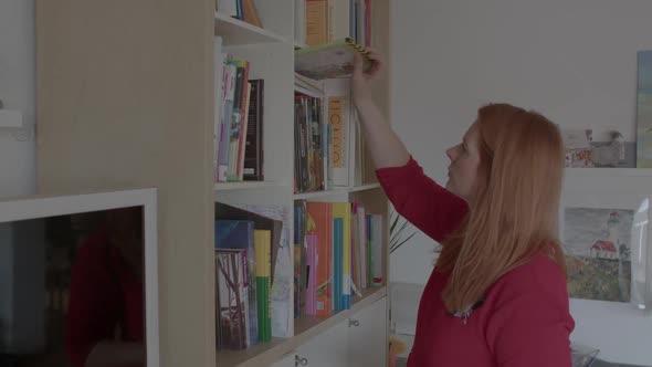 Woman Chooses a Book in Her Home Library