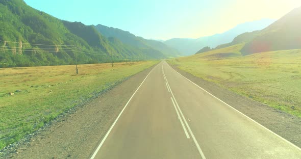 Aerial Low Air Flight Over Mountain Road and Meadow at Sunny Summer Morning.