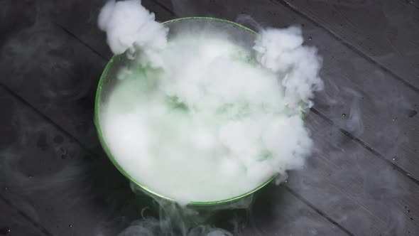 Green Liquid Boils Giving Off Smoke in a Glass Bowl on a Black Background