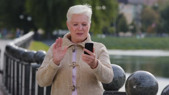 Overjoyed Senior Caucasian Woman Grandma Waving Hand Making Video Call Looking at Smartphone Camera