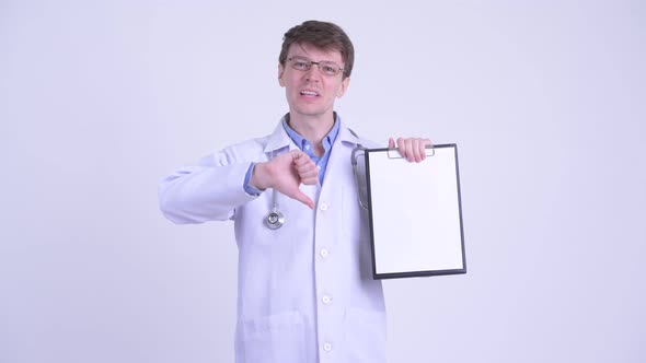 Serious Young Man Doctor Showing Clipboard and Giving Thumbs Down