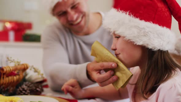 Caucasian senior man in santa hat wiping his daughter face with tissue sitting on dining table and e