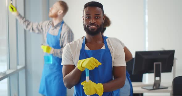 Portrait of African Cleaner in Apron and Gloves Holding Mop and Smiling at Camera Working in Office