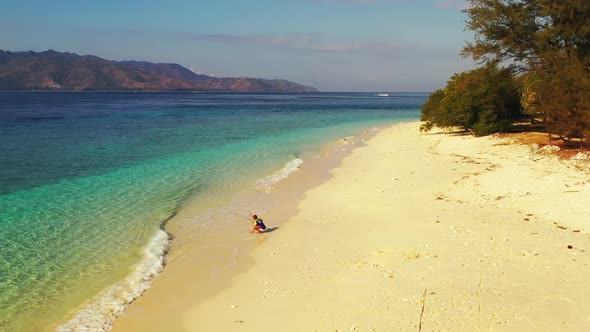 Single guy fishing alone on beautiful resort beach break by blue green sea with white sand backgroun