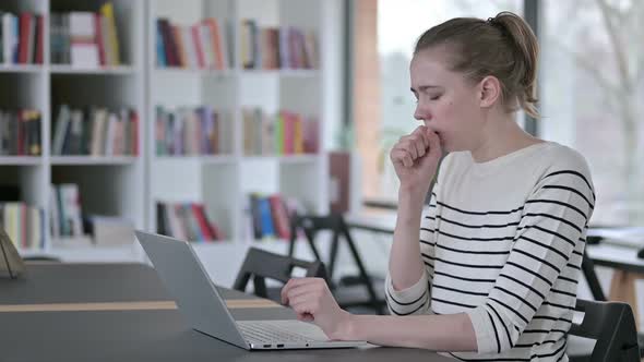 Serious Young Woman Using Laptop Coughing in Library