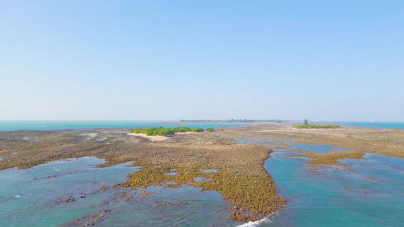 Ascending drone view of tropical island and beautiful blue water and coral reef, tilt up shot