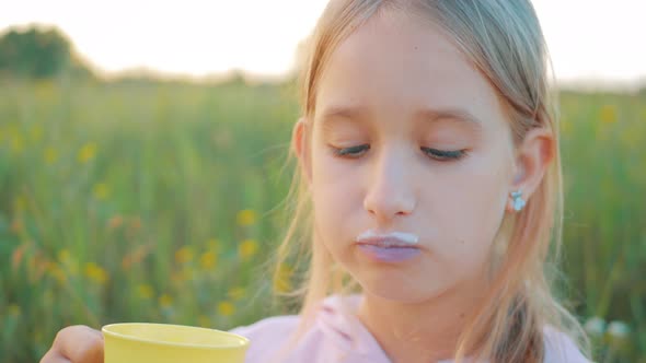 Cute Little Girl in the Field Eating a Bread and Drinking Milk at Sunset. Healthy Eating Concept