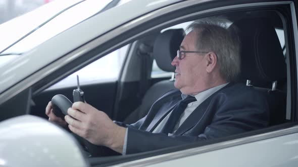 Close-up Portrait of Positive Mature Caucasian Man Looking Out the Car Window and Bragging Keys