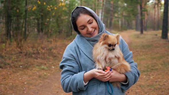 Young Woman Holding Pomeranian Mini Spitz in Arms While Walking in Autumn Park