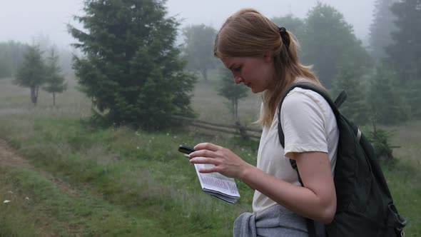 Young Girl Tourist with a Map and a Smartphone Device is Looking for the Direction of the Path to