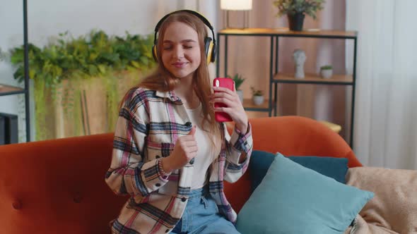 Overjoyed Young Woman in Wireless Headphones Dancing Singing on Cozy Couch in Living Room at Home