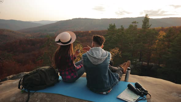 A Young Woman and Man are Sitting on a Large Rock and Drinking Tea