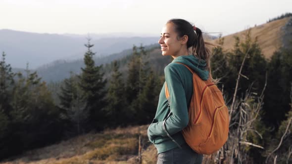 Woman Hiker Standing on Edge of Mountain Ridge Against Background of Sunset