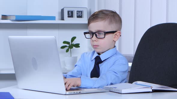 Boy in Glasses Is Typing on a Laptop and the Data Recorded in Notes