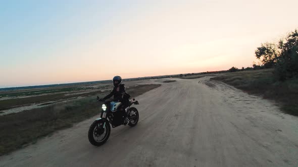 Young Stylish Woman Motorcyclist Driving Her Motorcycle in the Desert Road During Sunset