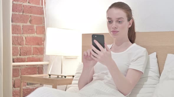 Attractive Redhead Young Woman Using Smartphone in Bed