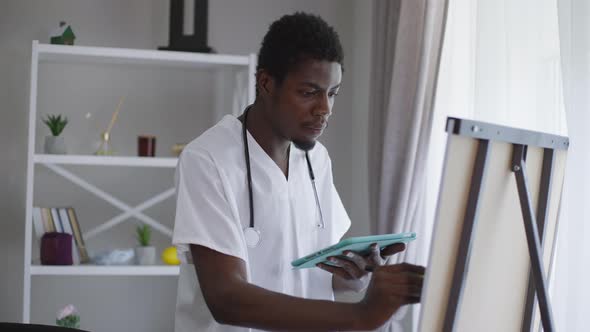 Medium Shot Smart African American Male Doctor Standing at Whiteboard with Tablet Writing with