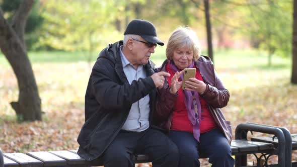 Happy Senior Couple Laughing and Exciting with Something in Smartphone Mobile While Sitting in the