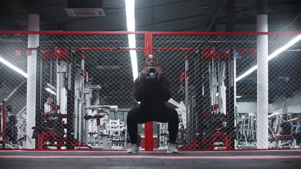 An Africanamerican Sportive Woman Squatting with Weight in a Gym