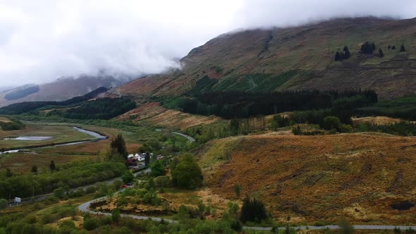 Cinematic drone shot of scottish highland village with river and misty mountains in background