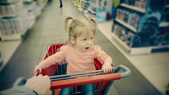 Little Child Sits in a Trolley Yawns His Parent Rolls Along Shelves with Goods in Store