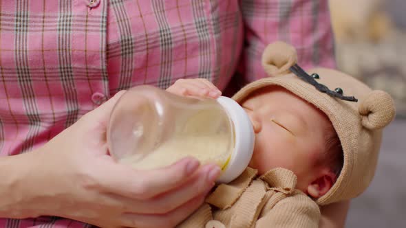 Newborn baby drinking milk from bottle on mom arms