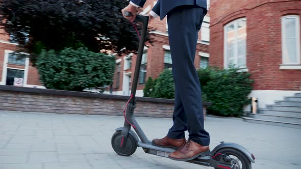 Unrecognisable Man in Business Suit Coming to Work on Electric Scooter